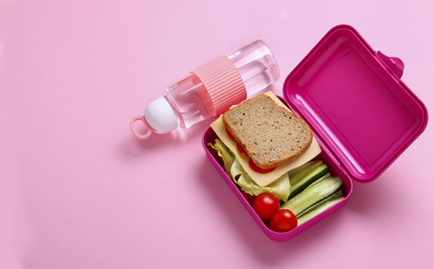 A healthy lunchbox with cheese and lettuce sandwich, tomato and cucumber on the side and a refillable waterbottle next to it.